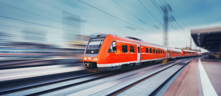 Das Bild zeigt einen Zug, der sich mit hoher Geschwindigkeit auf Gleisen bewegt und dabei Bewegungsunschärfe erzeugt, die die Geschwindigkeit des Zuges hervorhebt.