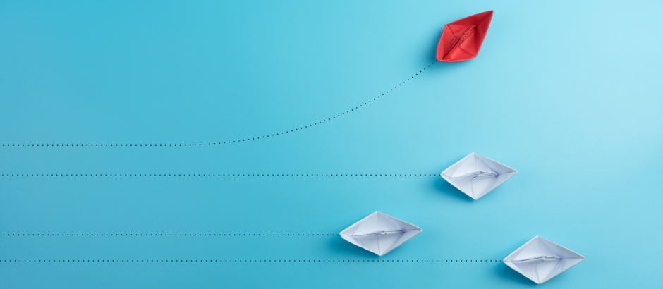 Das Bild, das ein rotes Papierschiffchen zeigt, das einen anderen Weg als die weißen Papierschiffchen einschlägt, symbolisiert Führung, Innovation und das Abweichen von der Norm