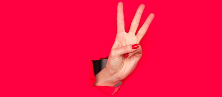 Das Bild zeigt eine Hand, die aus einem roten Hintergrund herausragt und drei Finger (Zeigefinger, Mittelfinger und Ringfinger) ausgestreckt hat, während Daumen und kleiner Finger eingezogen sind. Dies ist eine gängige Geste, um die Zahl Drei darzustellen.