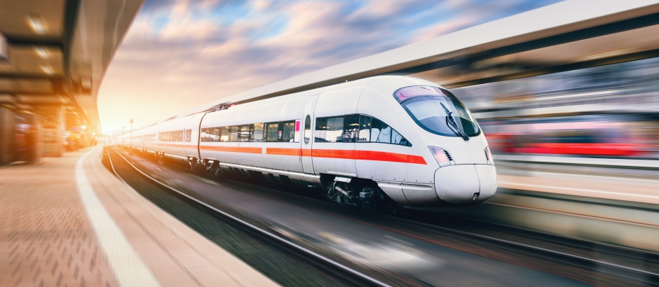 Ein moderner, grüner Zug fährt mit hoher Geschwindigkeit durch einen Bahnhof. Die Bewegung ist deutlich sichtbar durch verschwommene Linien im Hintergrund. Die Sonne scheint von links ins Bild und erzeugt eine warme, dynamische Atmosphäre – die Szene symbolisiert Fortschritt und Mobilität.