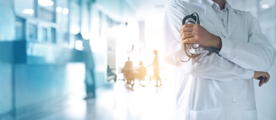 Arzt im Kittel, dahinter eine Krankenschwester mit einer pflegebedürftigen Person im Rollstuhl