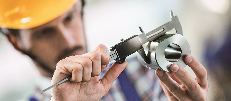 Closeup of metal processing plant worker inspecting certain pieces of finished products. He's making sure that the steel cylinder has proper dimensions. He's using manual caliper device.