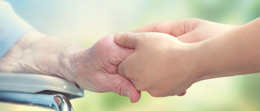Seniorin im Rollstuhl hält die Hand einer jungen Pflegekraft
