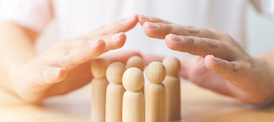 Konzept zum Schutz der Gesundheit von Menschen und zur Versicherung. Hand bildet einen schützenden Schild über einer Holzfigur auf dem Tisch.