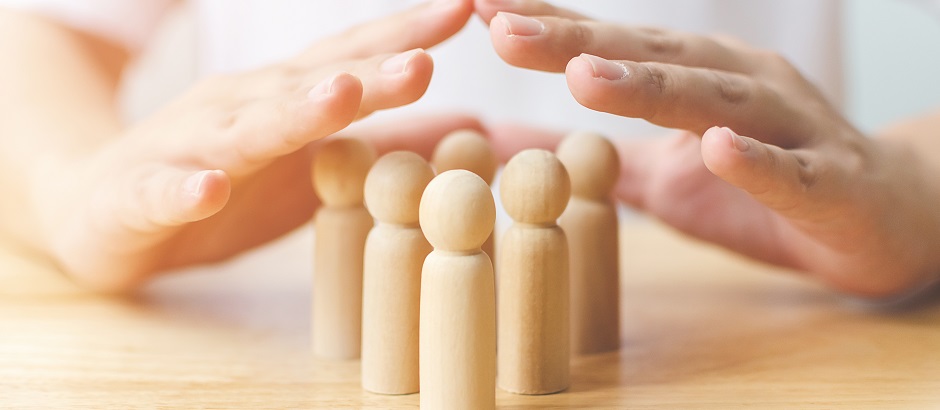 Konzept zum Schutz der Gesundheit von Menschen und zur Versicherung. Hand bildet einen schützenden Schild über einer Holzfigur auf dem Tisch.