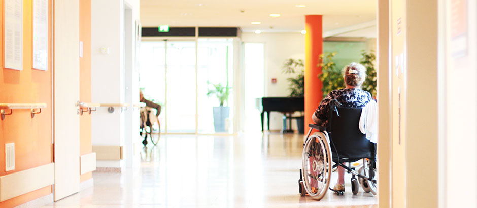 Bild von einem Korridor im Pflegeheim. Es sind zwei pflegebedürftige Patienten im Rollstuhl zu sehen.