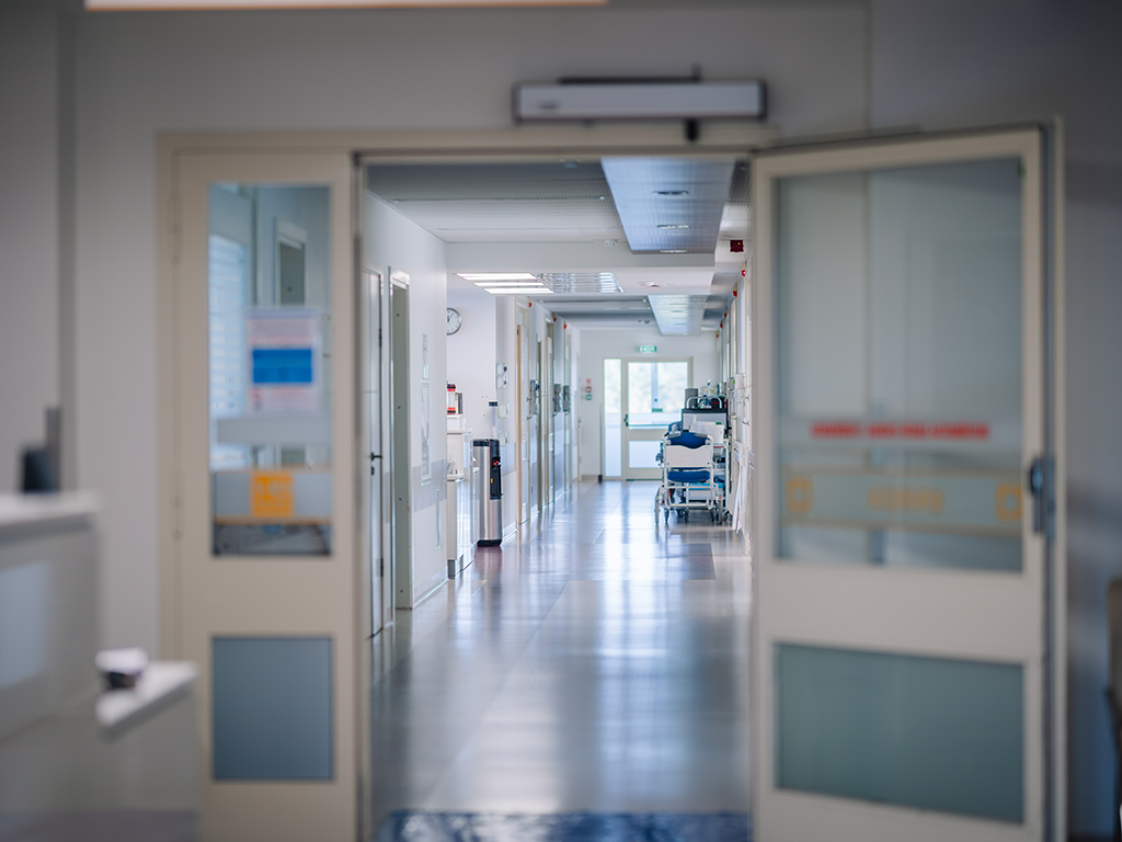 Der Korridor eines Krankenhauses. Es sind medizinische Apparate und mehrere Liegen zu sehen, ebenso ein Wasserspender.