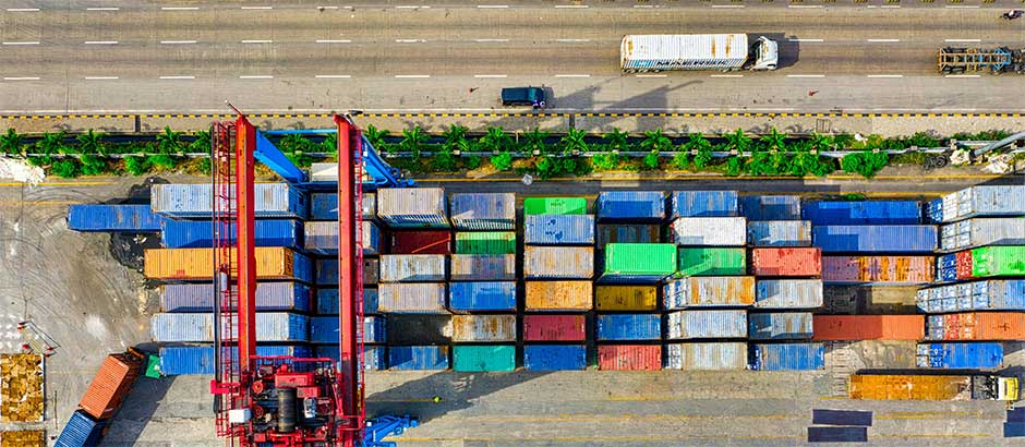Luftaufnahme eines Containerterminals mit farbigen Frachtcontainern und einem roten Kran – Symbol für moderne Transport- und Logistiklösungen.