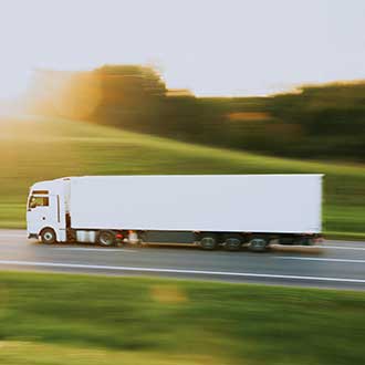 Weißer Lkw fährt mit leichter Bewegungsunschärfe über eine Landstraße bei Sonnenuntergang – Symbol für effiziente Transport- und Logistiklösungen.