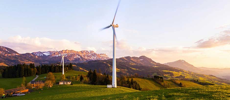 Windrad in einer grünen Berglandschaft bei Sonnenuntergang – Symbol für nachhaltige Energiegewinnung.
